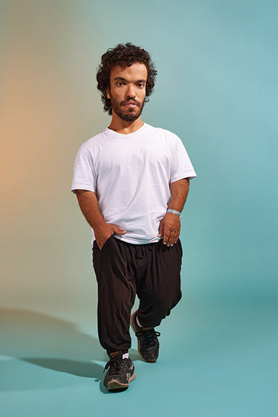 Ein junger Mann läuft lässig in Richtung Kamera. Er trägt Turnschuhe und ein weißes Shirt.