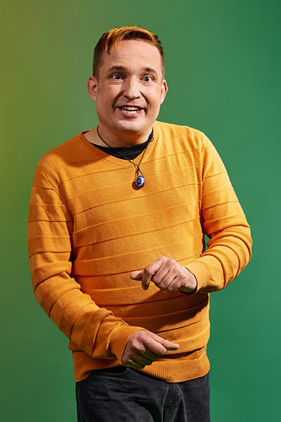 Ein junger Mann schnippt mit den Fingern und schaut aufgeweckt in die Kamera.
